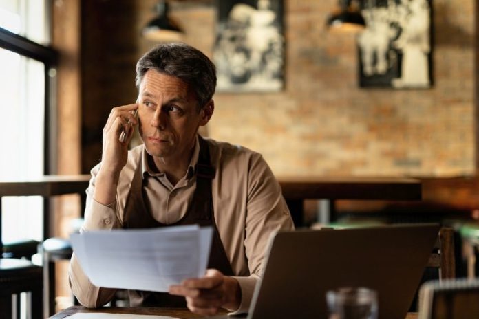 Mid adult waiter communicating on cell phone while analyzing pap